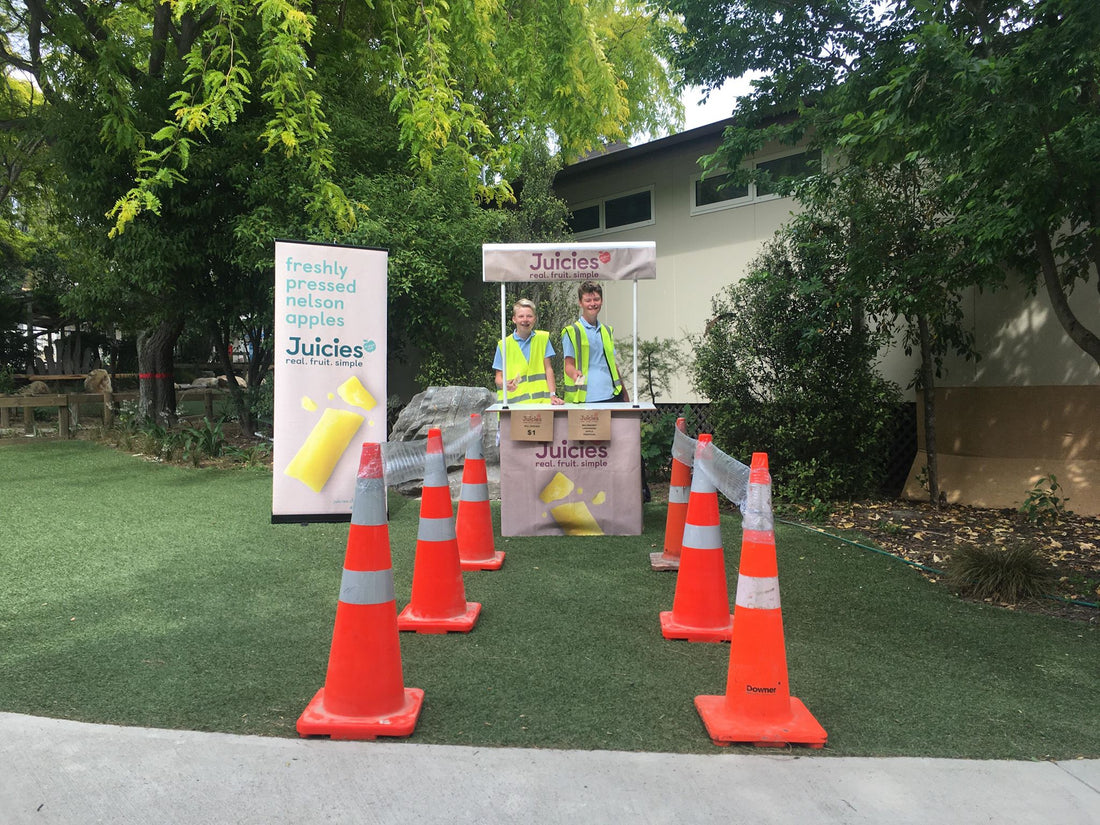 Two students ready to sell Juicies with Juicies shop outdoors, cones for line